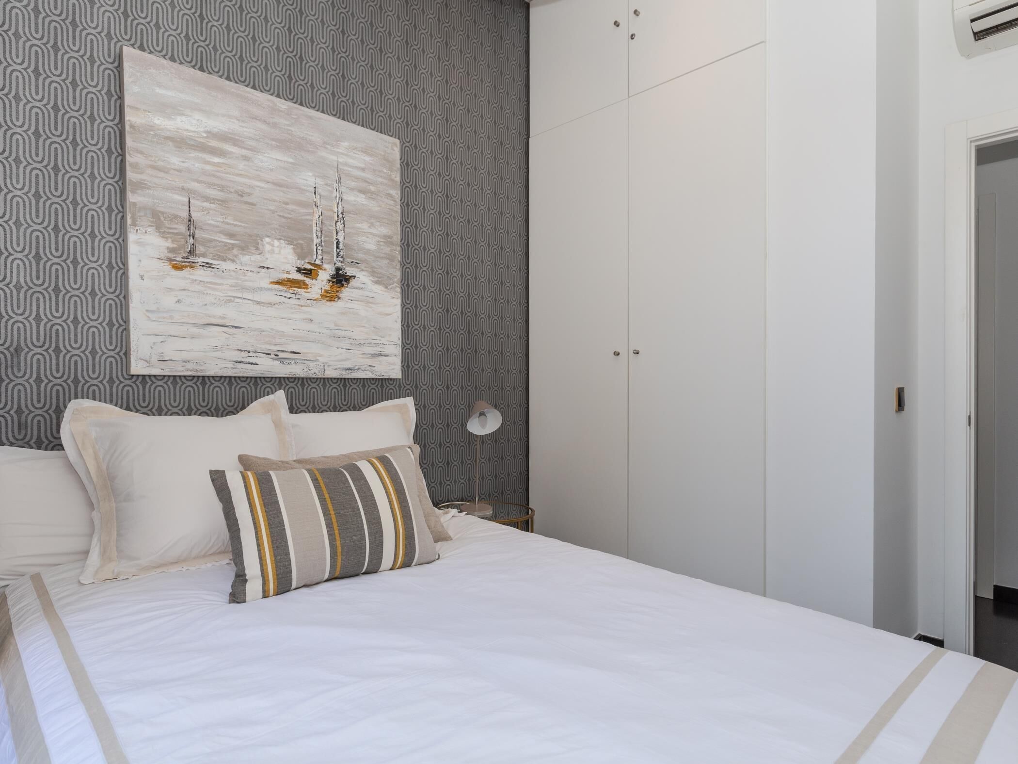 Une chambre à coucher avec un lit, des oreillers, un tableau accroché au mur, une armoire et un papier peint à motifs.