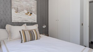 Ein Schlafzimmer mit einem Bett, Kissen, einem Wandbild, einem Kleiderschrank und einem gemusterten Wandteppich.