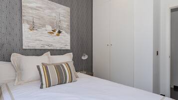 Une chambre à coucher avec un lit, des oreillers, un tableau accroché au mur, une armoire et un papier peint à motifs.