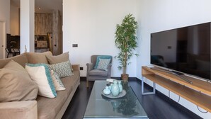 Ein modernes Wohnzimmer mit einer Couch, einem Sessel, einem Couchtisch, einem Fernseher und einer Zimmerpflanze.