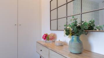 Une salle de bain avec un miroir, une commode agrémentée d’un vase de fleurs et un mur orné d’un motif.