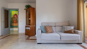A living room with a white sofa, a wooden cabinet, and a door with a colorful painting. - Bright apartment with terrace and parking in the center (Málaga)