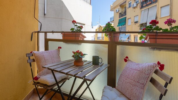 A balcony with a wooden table, two chairs, and potted plants. - Bright apartment with terrace and parking in the center (Málaga)