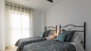 A bedroom with two beds, a ceiling fan, a bedside table with a lamp, and sheer curtains. - Bright apartment with terrace and parking in the center (Málaga)