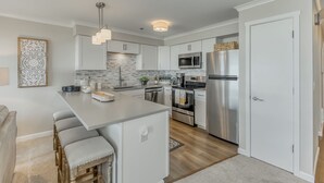 A modern kitchen with white cabinets, stainless steel appliances, and a central island with bar stools. - Oceanfront 3rd floor Balcony 2 blocks to Turnaround-Work Remotely (Seaside)