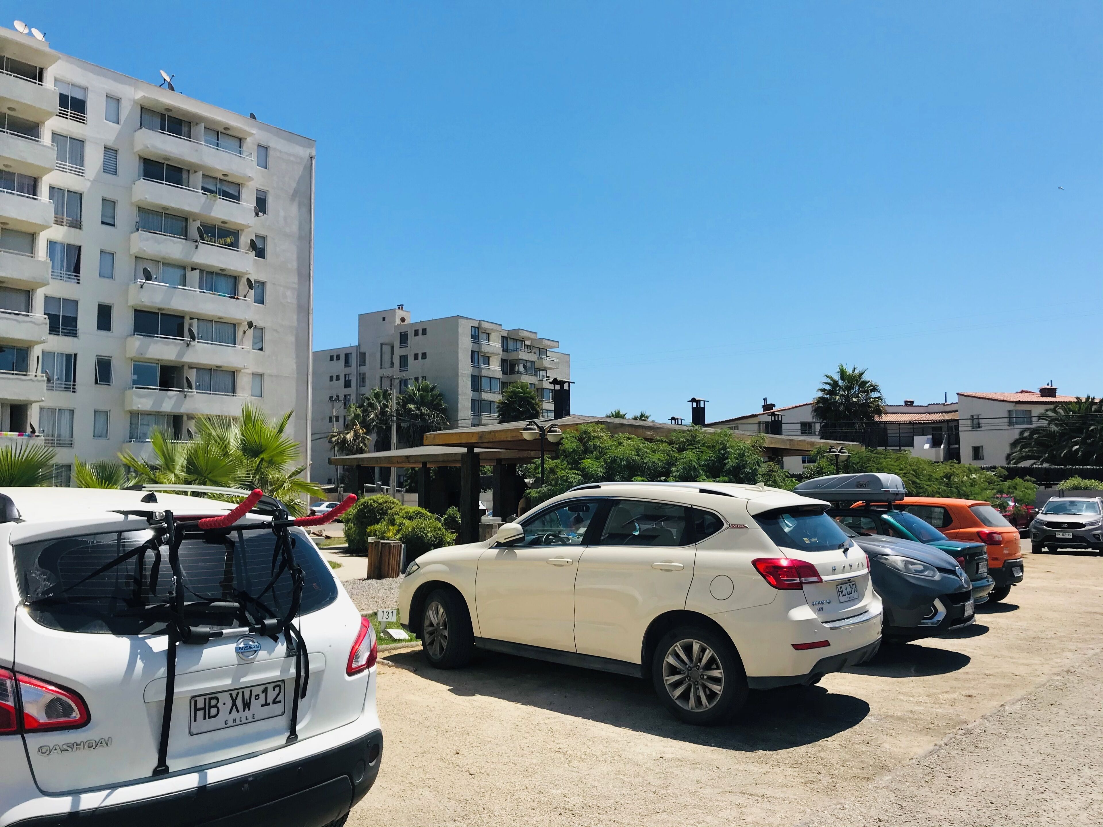 Parkkipaikalla oli useita autoja, muun muassa valkoinen Nissan Qashqai ja valkoinen maasturi, jotka oli pysäköity kerrostalon eteen. Kerrostalossa oli parvekkeita ja satelliittiantenneja.