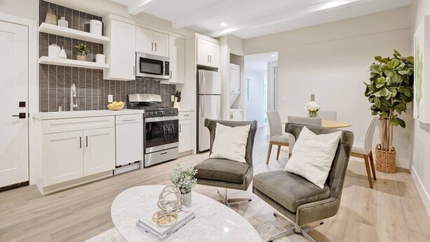 Una cocina moderna con armarios blancos, un microondas integrado y una estufa. Hay dos sillones grises y una mesa de centro redonda con un jarrón de flores.