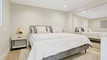 A modern bedroom with a large bed, a nightstand, a mirror, and a wooden floor.