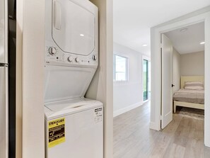 Laundry room with a front-loading washer and dryer, conveniently located near a bedroom with a bed.