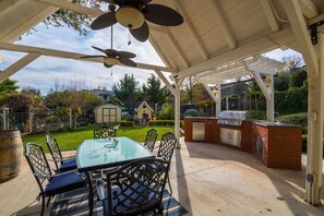 An outdoor patio with a glass table and chairs, a ceiling fan, and a barbecue grill.