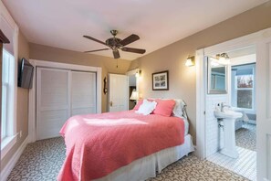 A bedroom with a bed, a ceiling fan, a bathroom with a sink and mirror, and patterned flooring.