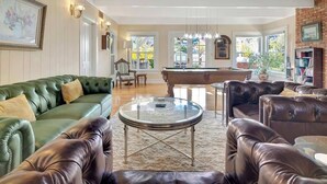 Ein geräumiges Wohnzimmer mit einem grünen Ledersofa, einem braunen Ledersessel, einem Glastisch und einem Billardtisch.