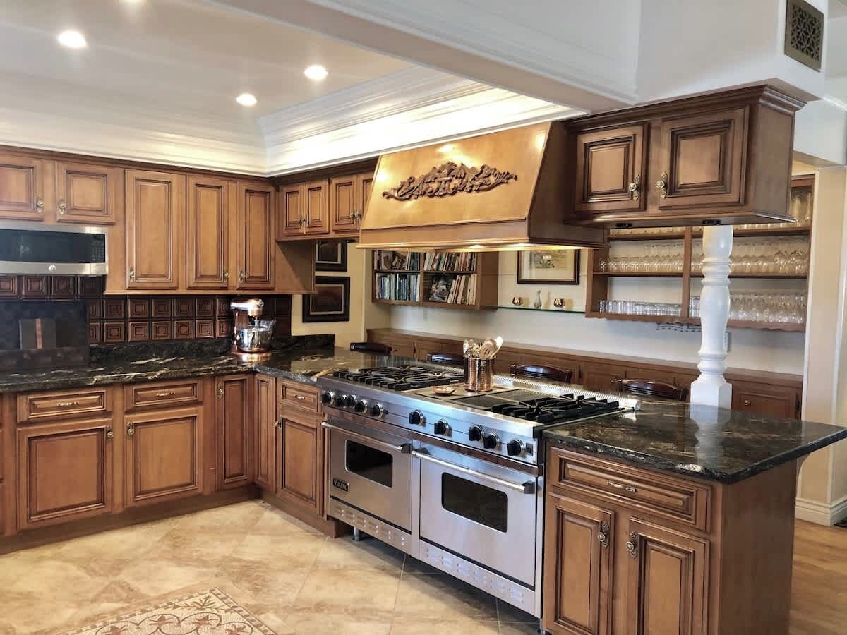 A spacious kitchen with wooden cabinets, a stainless steel stove, and a marble countertop.
