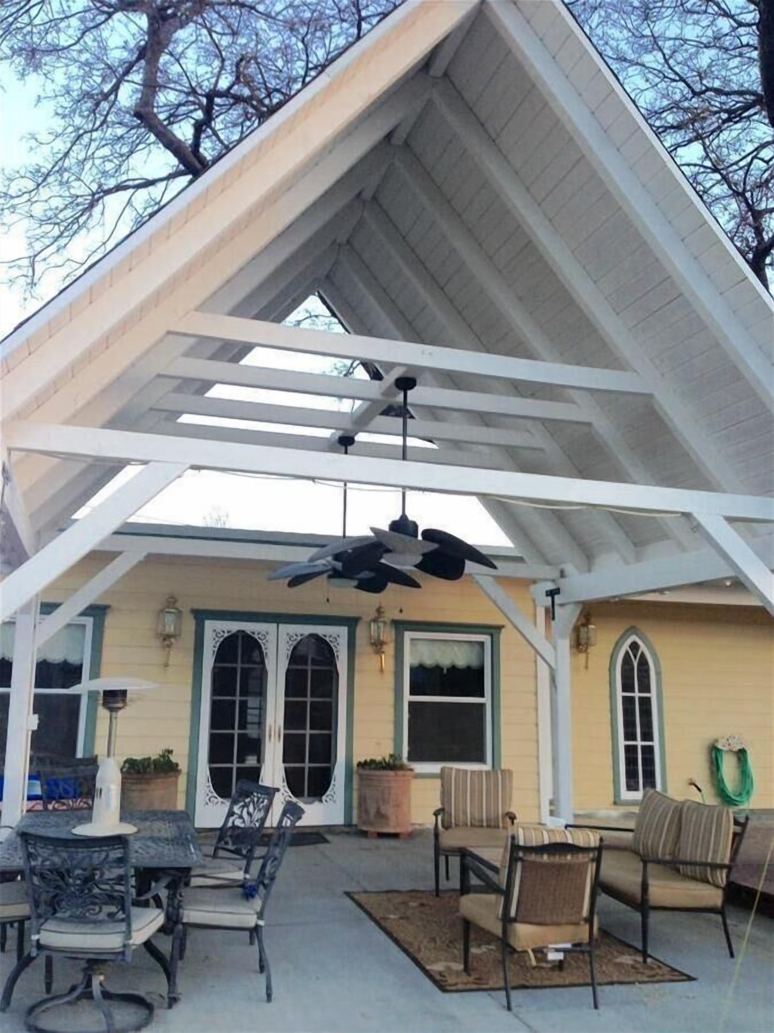 A covered patio area with outdoor furniture, including chairs and a table, under a white roof structure.
