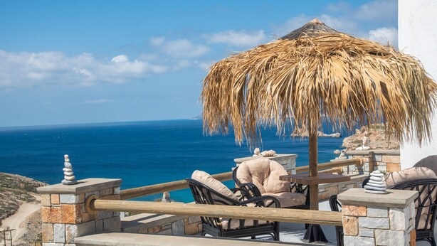 A seaside terrace with a thatched umbrella, stone railings, and lounge chairs overlooking the ocean.