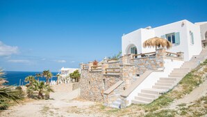 A white building with stone steps leading to a balcony, overlooking a coastal area.