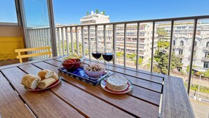 Un balcón con una mesa dispuesta para una comida, que incluye pan, un bol de frutos secos y un queso, con vistas a la ciudad de fondo.