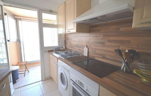 A kitchen with wooden cabinets, a built-in oven, a washing machine, and a window with a view. - Cannes center - very practical - all comfort (Cannes)