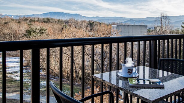 Een balkon met een tafel, een stoel en een kop koffie.