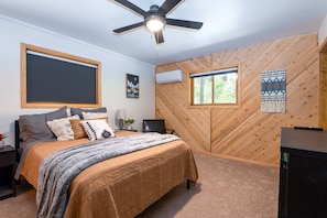 A bedroom with a bed, a ceiling fan, a window, and a wooden wall panel.