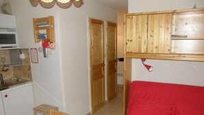 A compact kitchen with a microwave, wooden cabinets, a red sofa, and a small wooden table. - 2-room apartment, 4 pers, SE, balcony, collective parking (Valloire)
