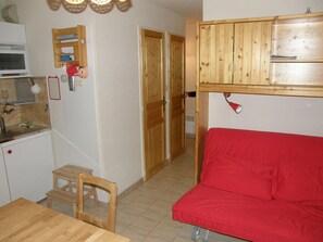 Eine kleine Küche mit Mikrowelle, Holzschränken, einem roten Sofa und einem kleinen Holztisch.