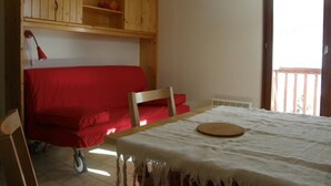 A room with a wooden cabinet, a red sofa, a table with a white tablecloth, and a window with a view. - 2-room apartment, 4 pers, SE, balcony, collective parking (Valloire)