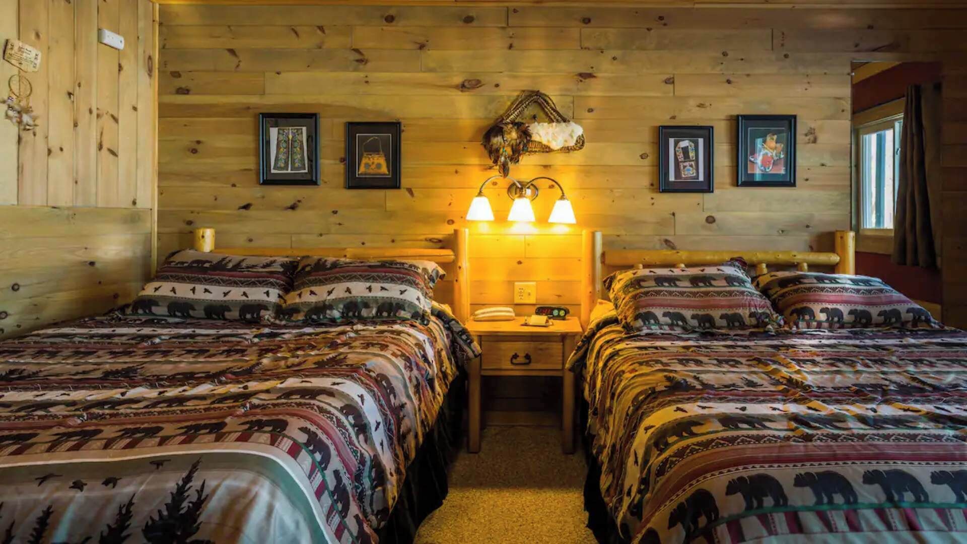 Quarto com duas camas, paredes de madeira e quadros emoldurados.