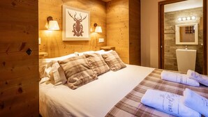 Quarto com painéis de madeira, uma cama, duas luminárias fixadas na parede e uma obra de arte com um veado emoldurado.