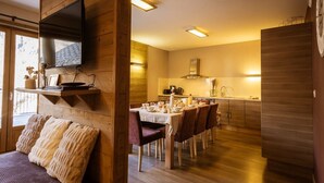 Um interior acolhedor com uma área de refeições de madeira, uma cozinha com eletrodomésticos modernos e uma TV de tela plana na parede.