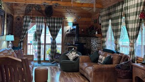 A cozy cabin interior with a wooden ceiling, plaid curtains, a leather sofa, and a stone fireplace.