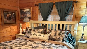 A cozy wooden bedroom with a bed, a nightstand, a lamp, and a sign that reads "Always Kiss Me Goodnight".