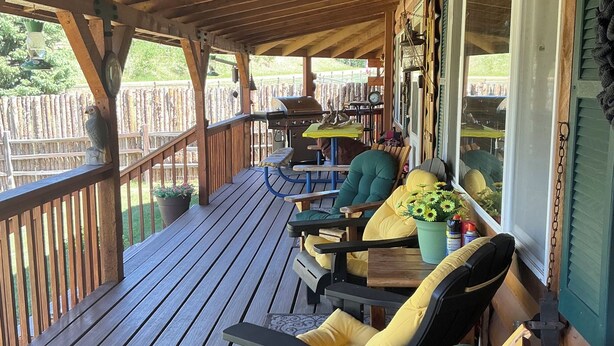 A wooden deck with outdoor seating, a grill, and a view of the outdoors.