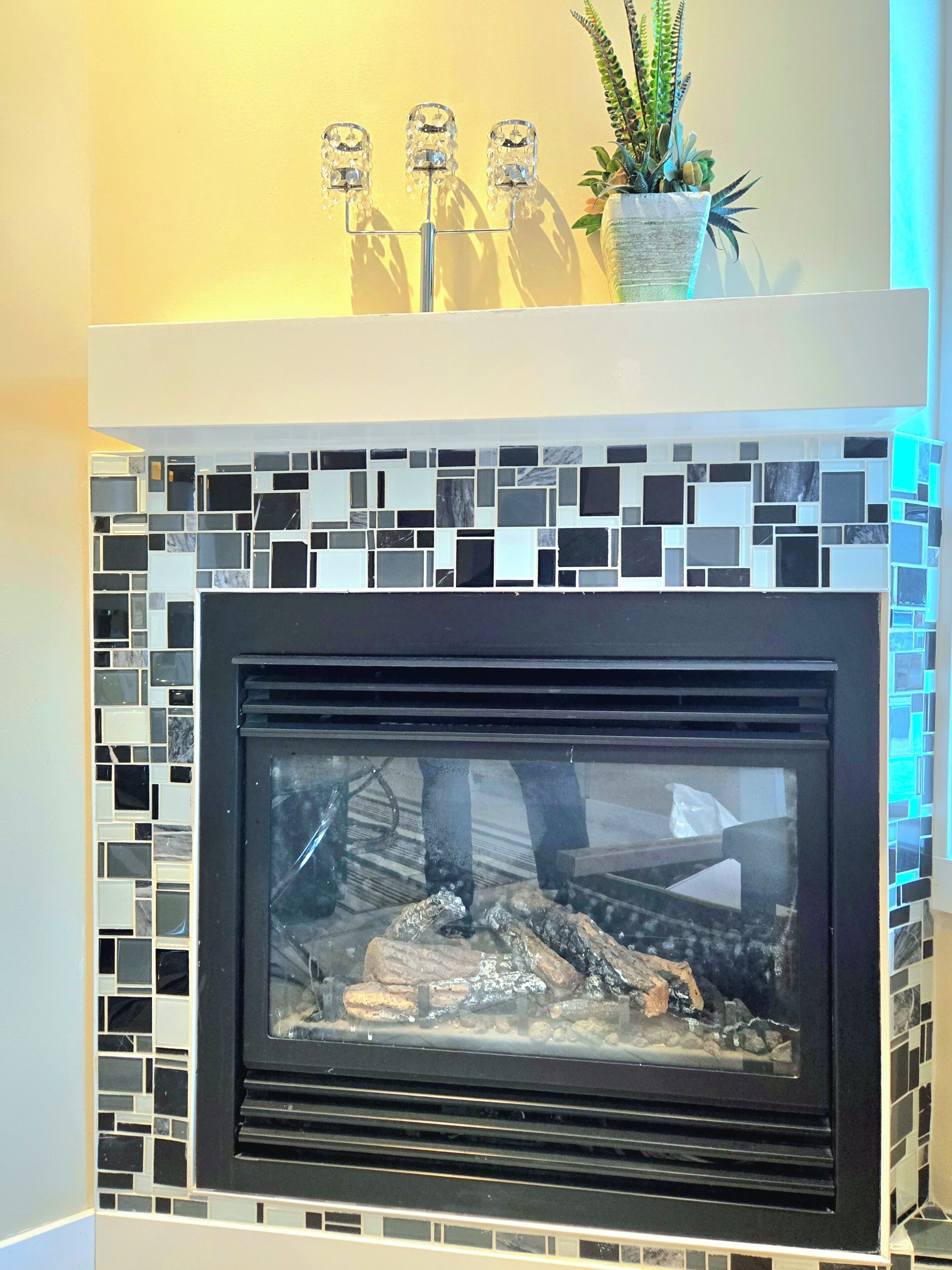 Une cheminée ornée d’un décor en mosaïque, une plante en pot et un luminaire décoratif placé au-dessus.