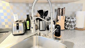 A modern kitchen with a stainless steel sink, a flexible faucet, a toaster, a bottle of olive oil, and a knife block.