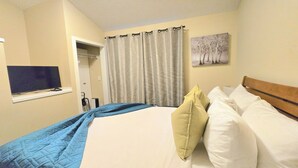 A hotel room with a bed, a television on a shelf, a painting on the wall, and a door leading to a bathroom.