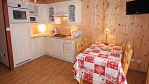 A compact kitchen with white cabinets, a microwave, a stove, and a dining table with a red and white tablecloth. - Duplex 3 rooms 4 people, south-facing terrace, private parking (Valloire)