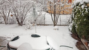 A snow-covered garden with a wooden fence, a metal pole, and a building with red windows in the background. - Duplex 3 rooms 4 people, south-facing terrace, private parking (Valloire)