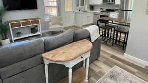 A modern kitchen with white cabinets, a microwave, and a refrigerator. There is a gray sofa with a wooden coffee table in the living area.