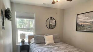 A bedroom with a bed, a window, a nightstand, a lamp, a ceiling fan, and a framed picture on the wall.