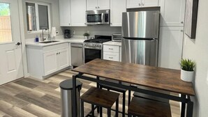 A modern kitchen with white cabinets, stainless steel appliances, a wooden dining table, and a trash can.