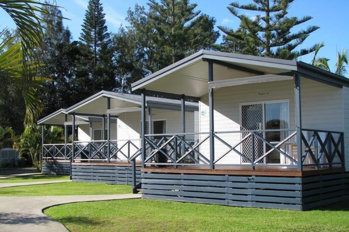 Een rij twee verdiepingen tellende bungalows met een overdekte veranda, omgeven door grasvelden en bomen.