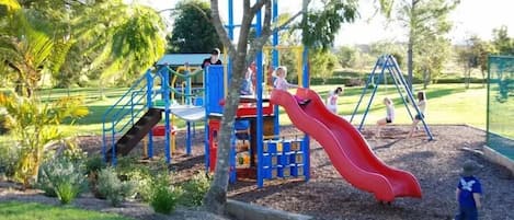 A playground with a red slide, climbing structures, and a fenced area.