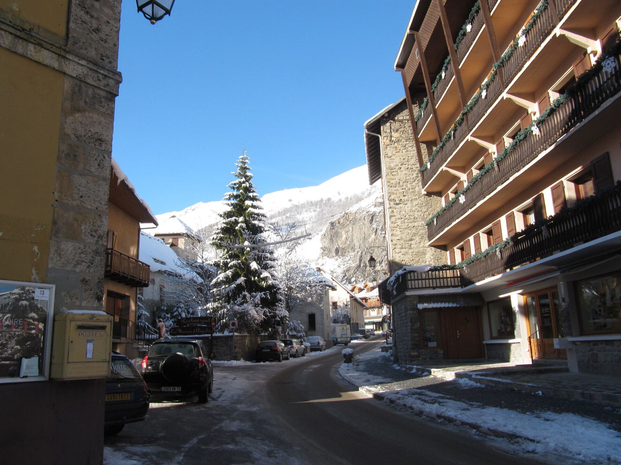 A snow-covered street with buildings, a Christmas tree, and a mountain in the background.