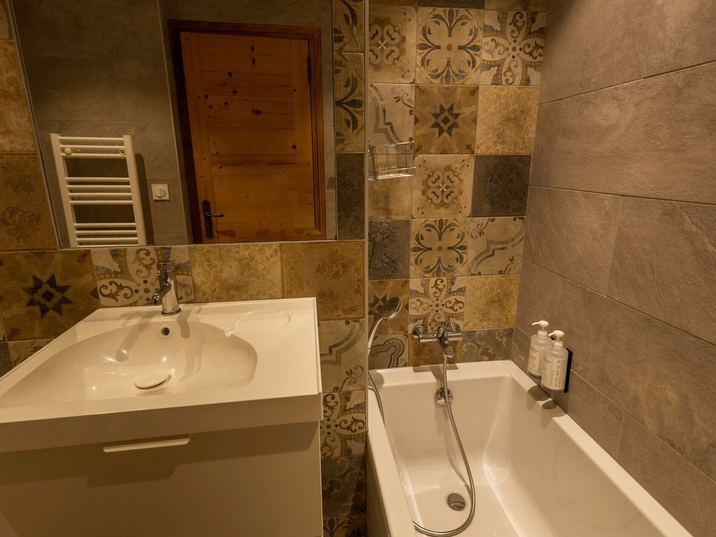 A bathroom with a white sink, a bathtub, and patterned tiles on the walls.