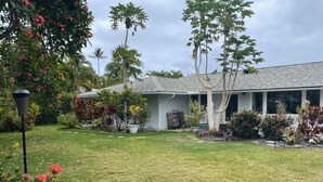 Una propiedad residencial con un césped cuidado, una variedad de plantas tropicales y una casa con techo gris.