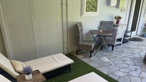 Un patio amueblado con una zona de estar que incluye un sofá y sillones, una mesita con una planta en maceta y suelo de baldosas de piedra.