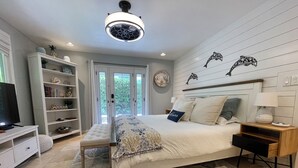 Un dormitorio con cama, mesita de noche, lámpara y una estantería con libros y objetos decorativos.