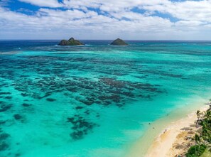 Una playa tropical con aguas turquesas cristalinas, una orilla arenosa y dos islas pequeñas a lo lejos.