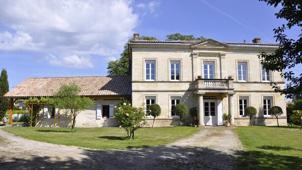 Un ampio edificio in pietra di due piani, con una facciata simmetrica, un ingresso centrale con un balcone e una strada di ghiaia che conduce all'ingresso.